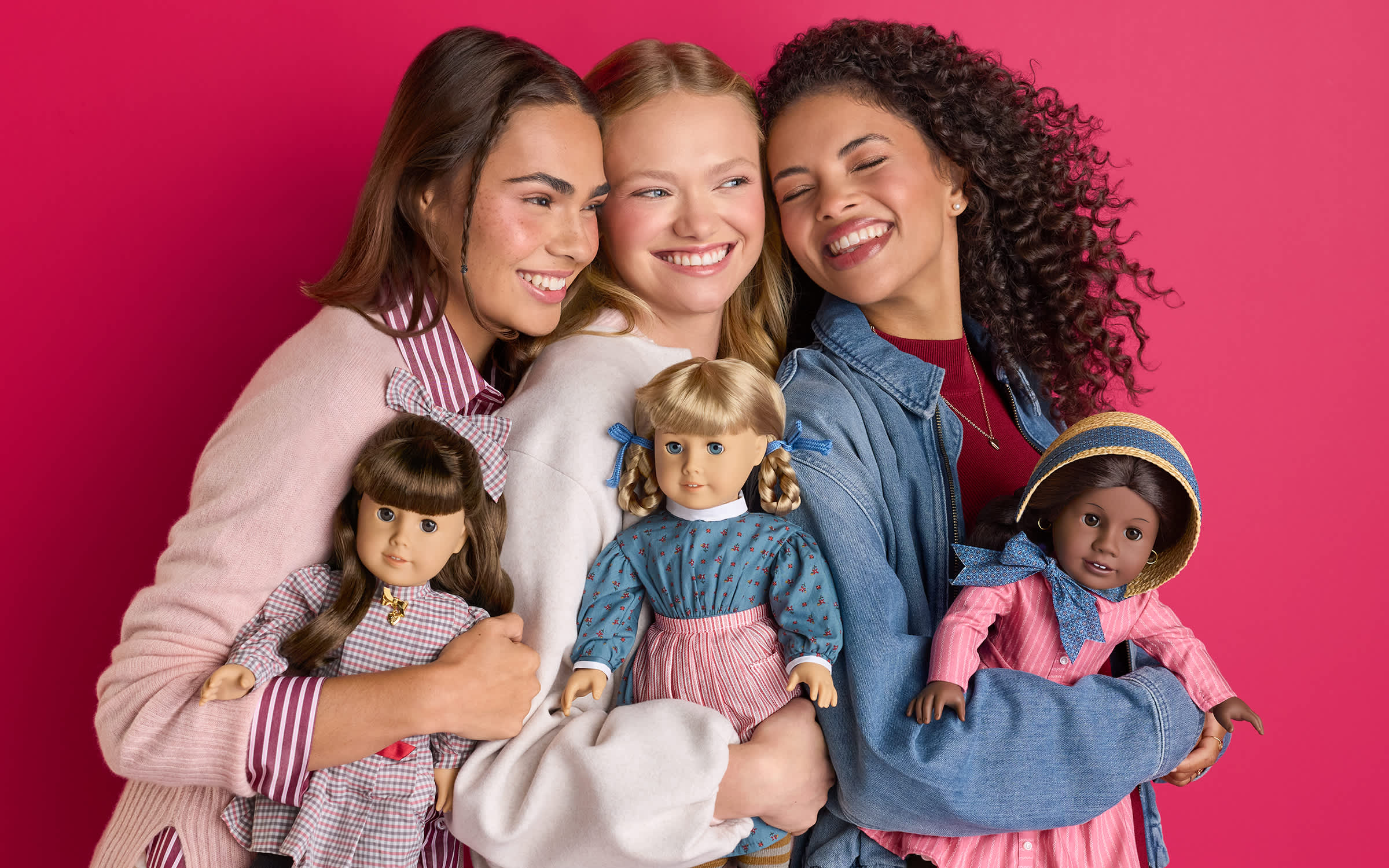 Three women standing together and smiling while holding Samantha, Kirsten, and Addy dolls